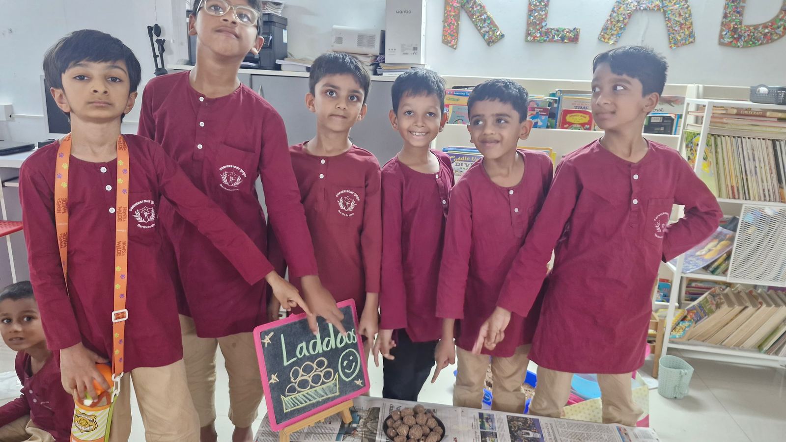 Five Grade 2 children in maroon kurtas stand shoulder to shoulder at the laddoo stall they ran