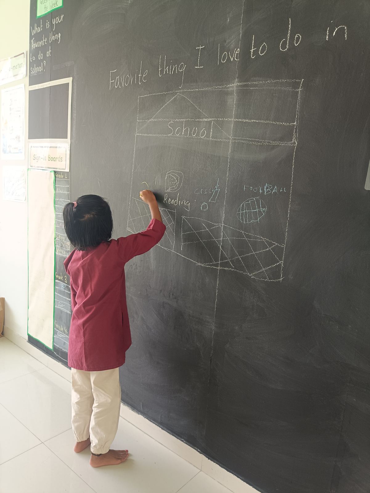 A girl in a maroon kurta draws on the blackboard