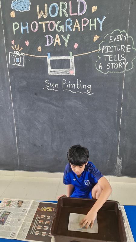 A boy makes a sun print under a World Photography Day board