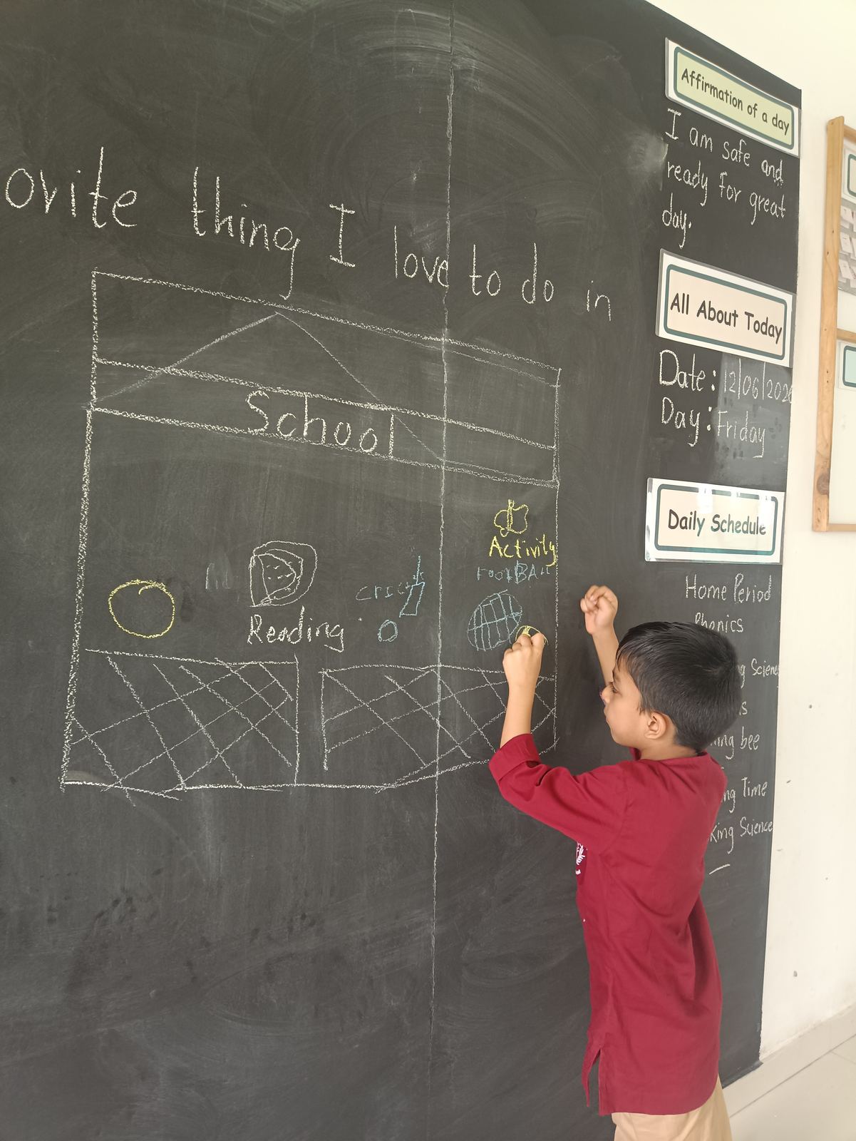 A child in a maroon kurta writes on the blackboard in her own hand