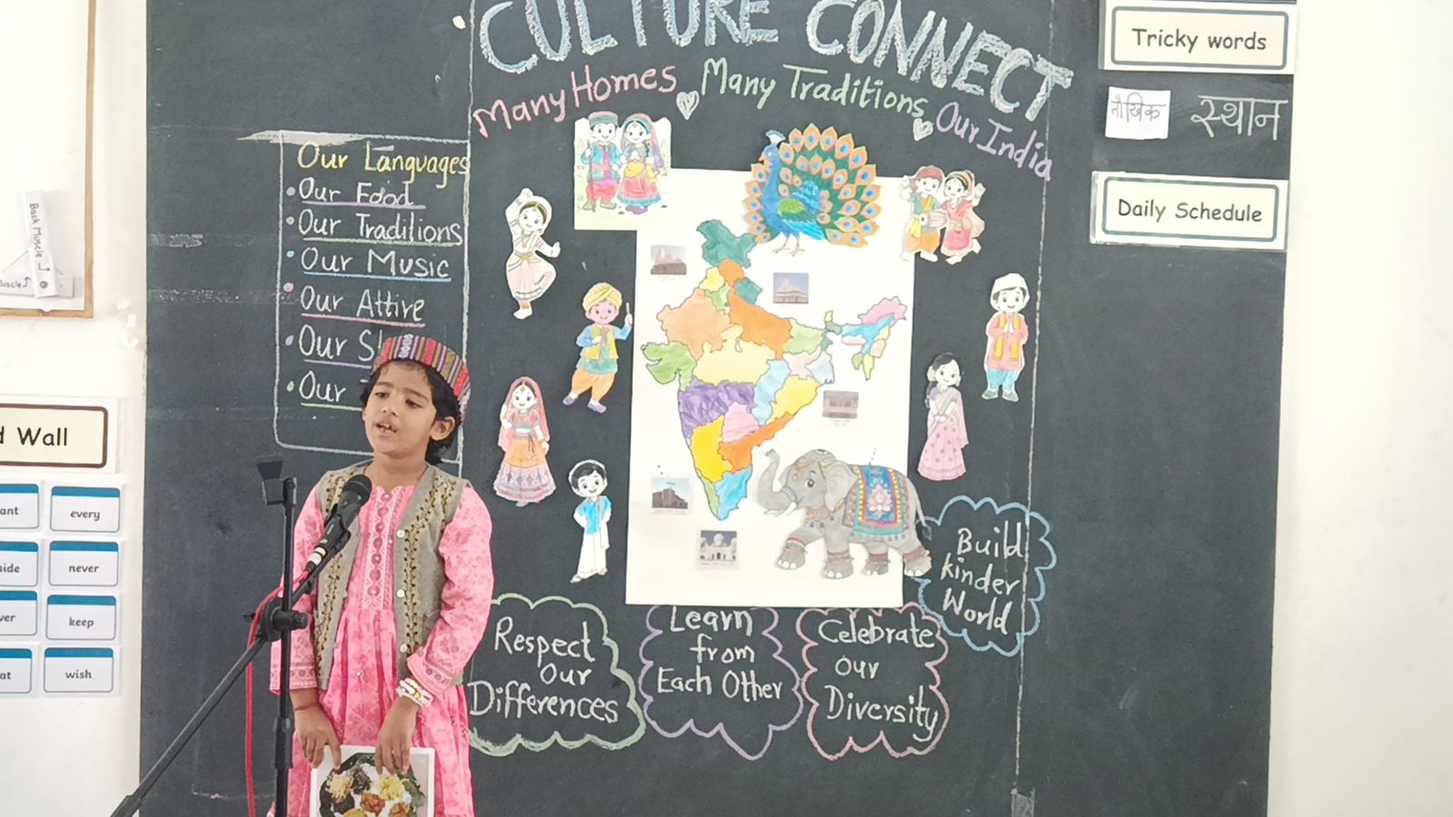 A girl in a pink dress sings into a microphone in front of the Culture Connect board