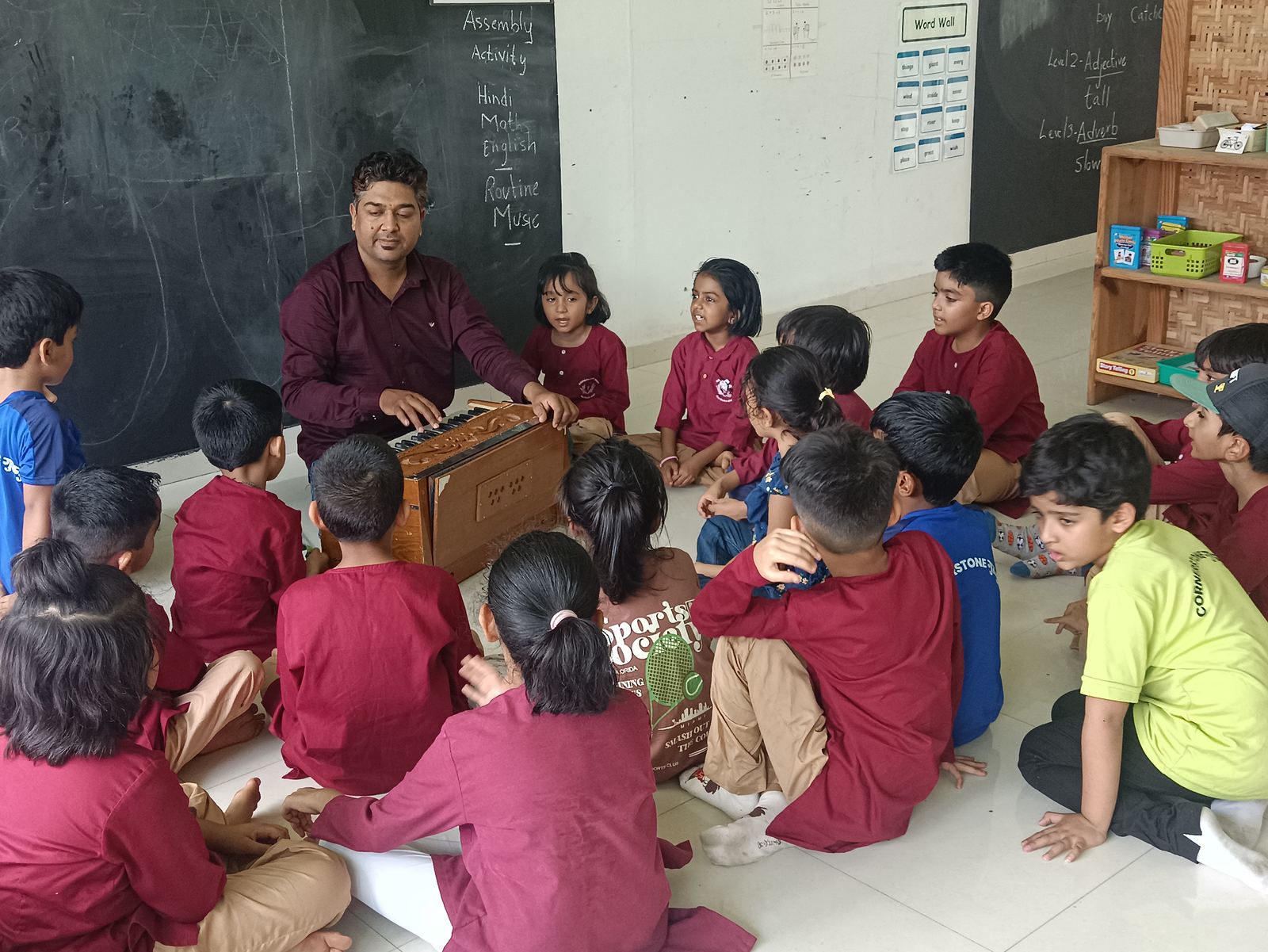 A teacher plays the harmonium for a circle of children seated on the floor