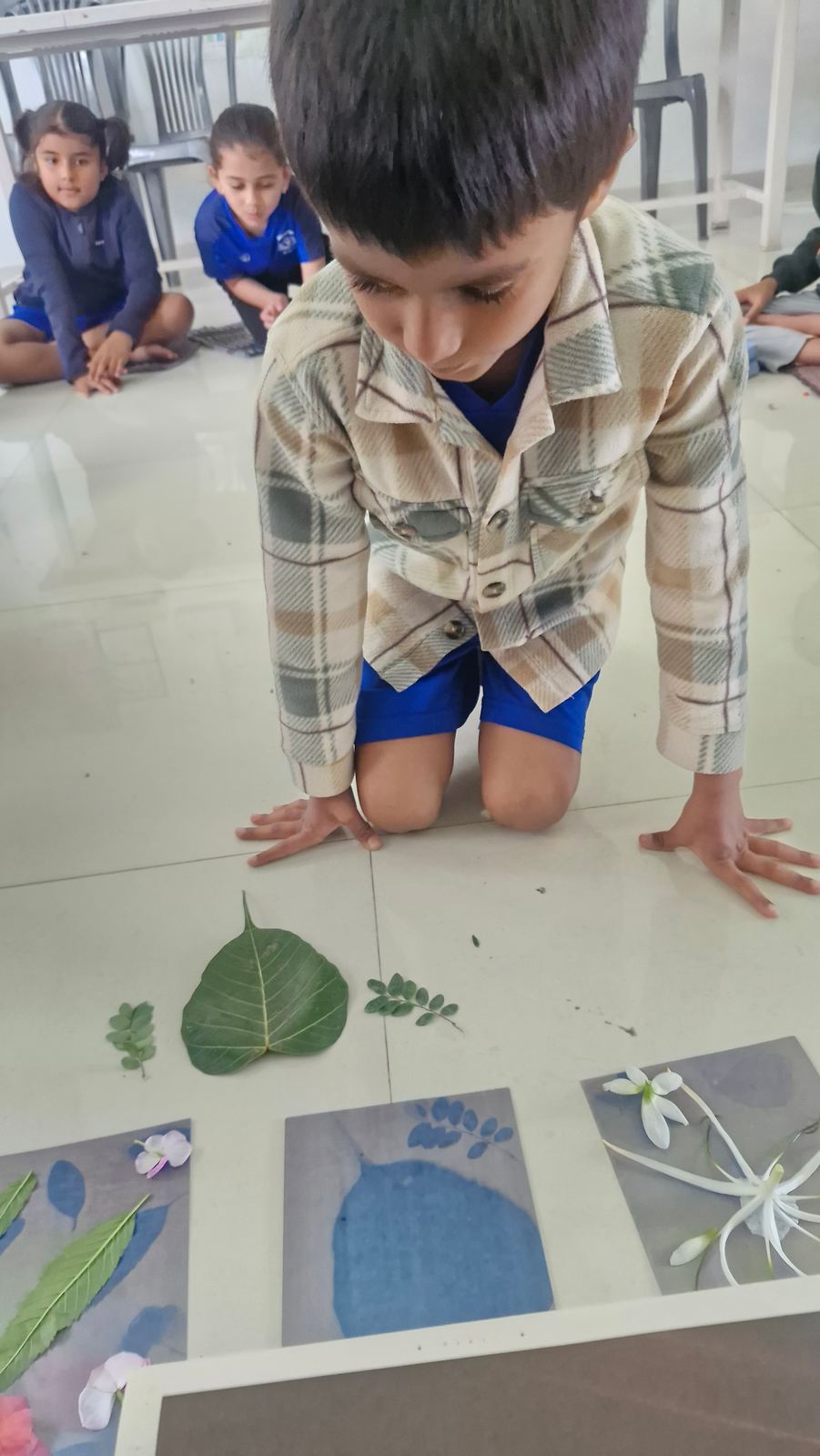 A boy kneels over leaf prints laid out on the floor