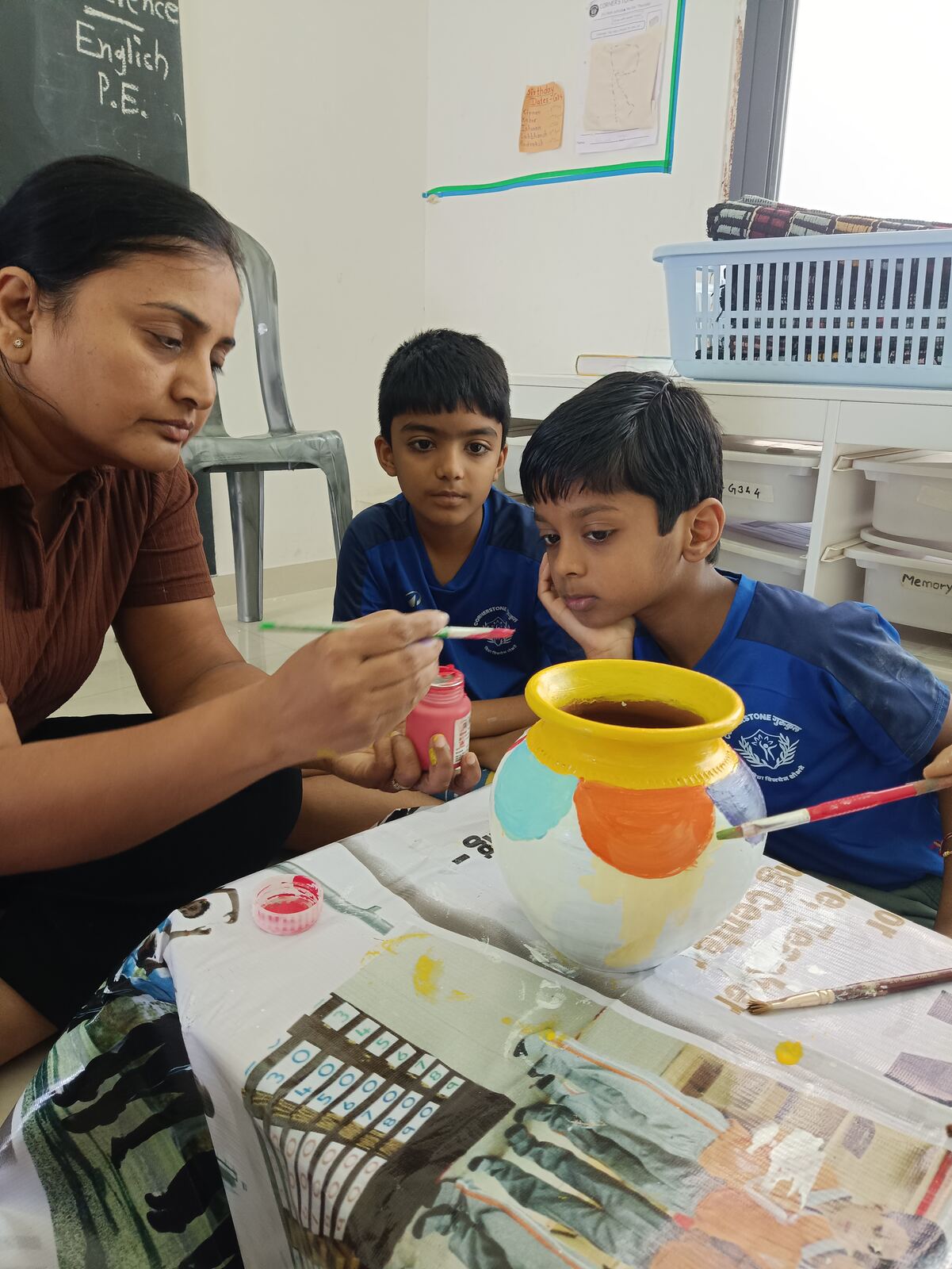 A teacher paints a pot with two boys